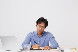 Seorang lelaki tengah duduk sambil menulis copywriting untuk mempelajari skill digital marketing